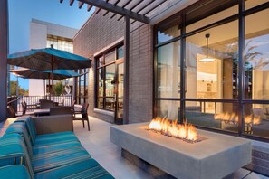 Un espacio de estar al aire libre con una chimenea, ventanas amplias y una pérgola.
