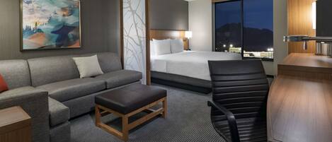 A hotel room with a bed, a sofa, a desk, and a chair.