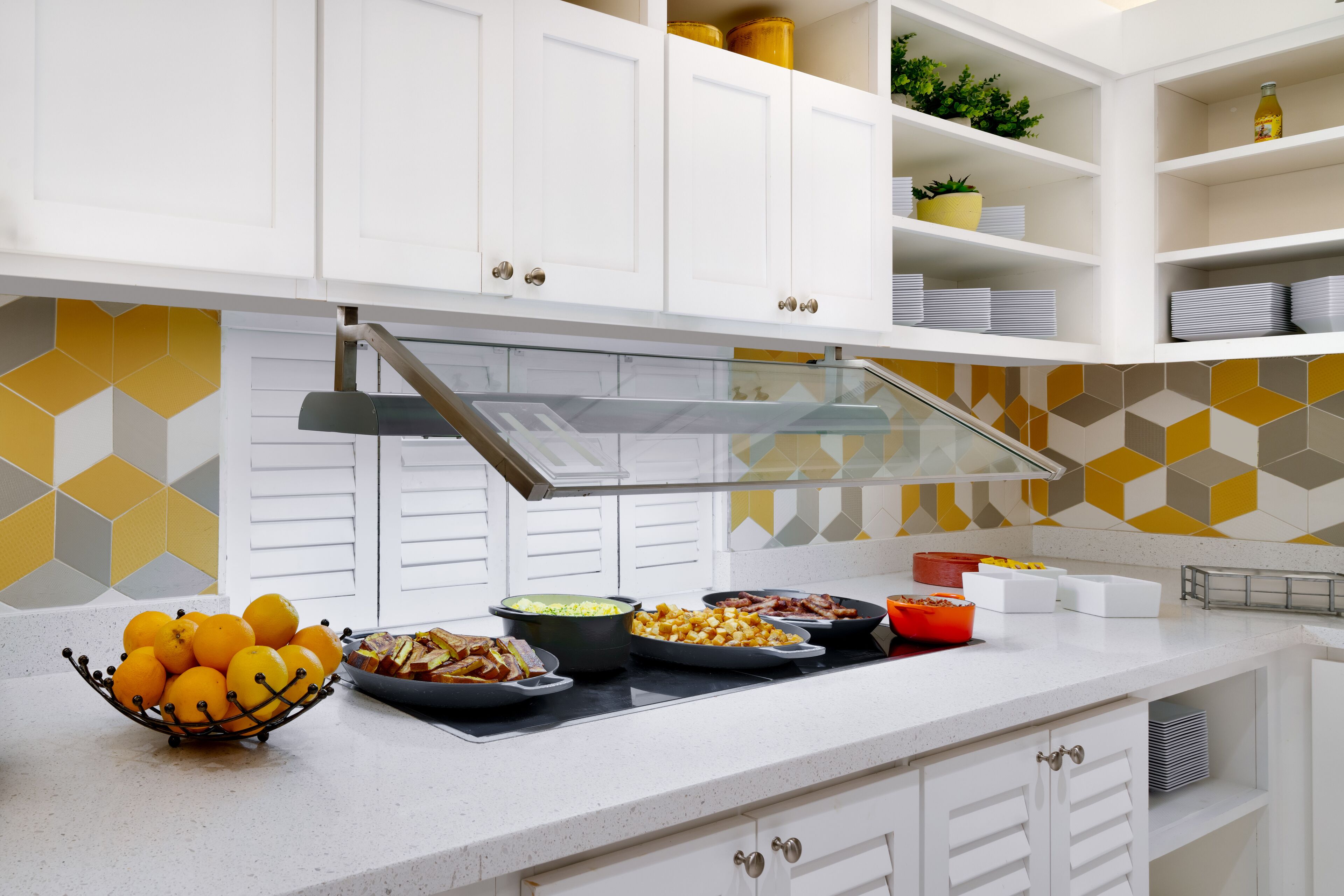 A modern kitchen with white cabinets, a stainless steel range hood, and a variety of food items on the counter.