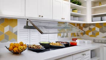 A modern kitchen with white cabinets, a stainless steel range hood, and a variety of food items on the counter.
