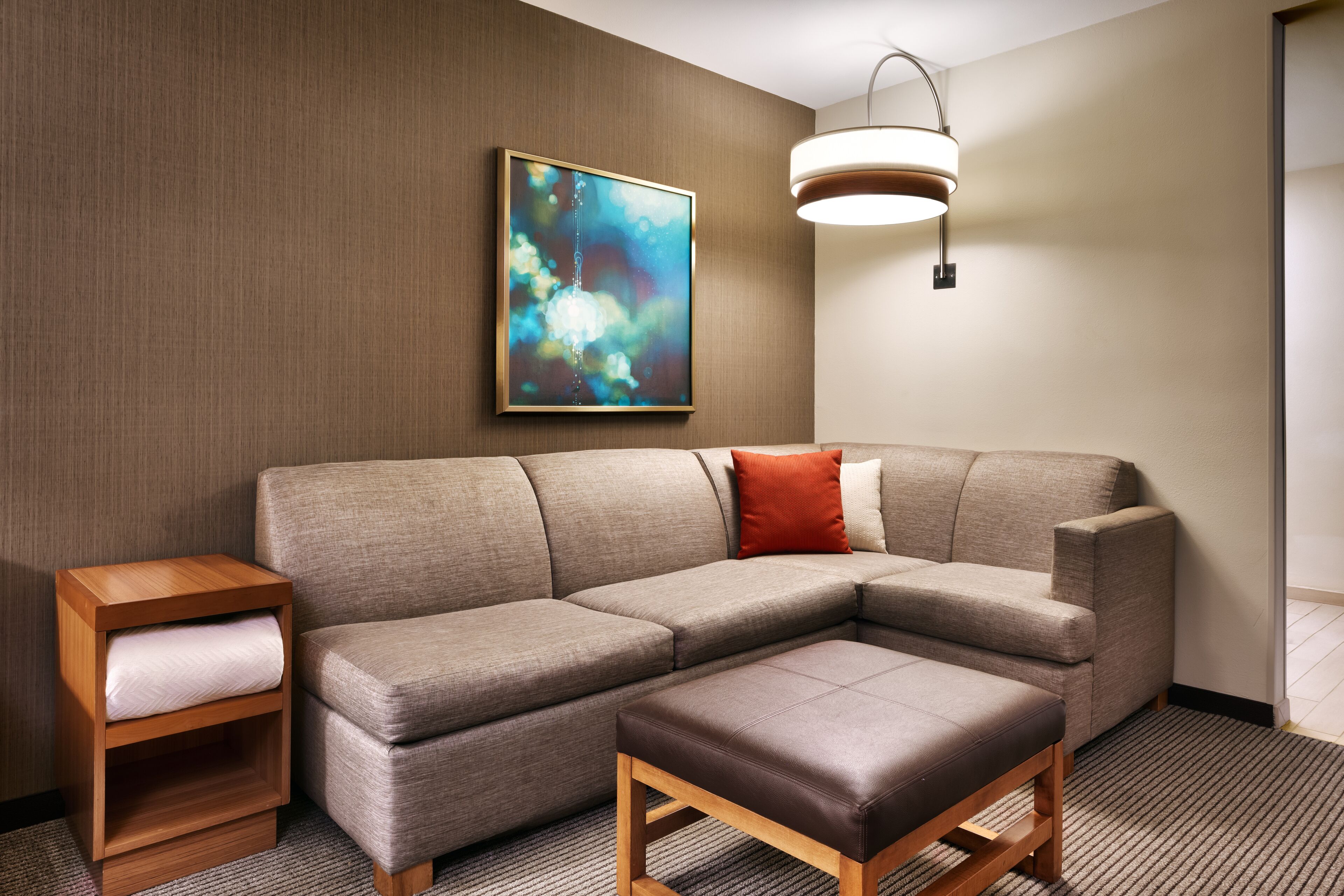 A modern living room with a sectional sofa, a wooden side table with a cushion, a bench, and a wall-mounted abstract painting.