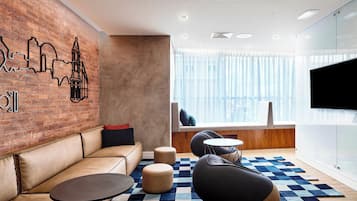 Un salón moderno con pared de ladrillo, sofá de cuero, mesas redondas y alfombra a cuadros.