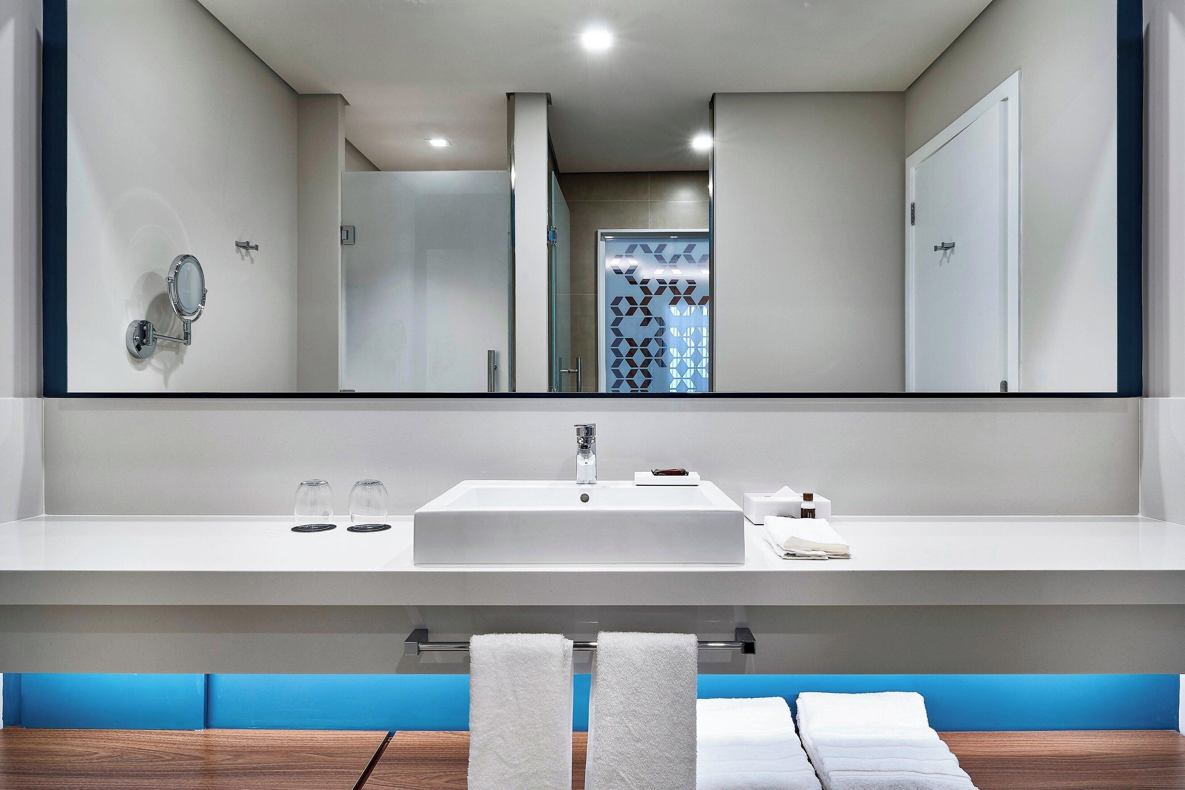 A modern bathroom with a large mirror, white sink, and two towels on a rack.