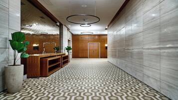 A modern hallway with a geometric patterned floor, wooden reception desk, and a large potted plant.