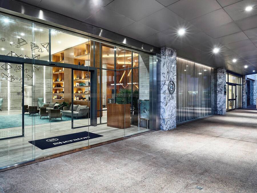 A modern hotel lobby with a glass facade, wooden interior, and a marble column.