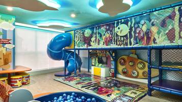 Zona infantil con tobogán, piscina de pelotas y murales coloridos.