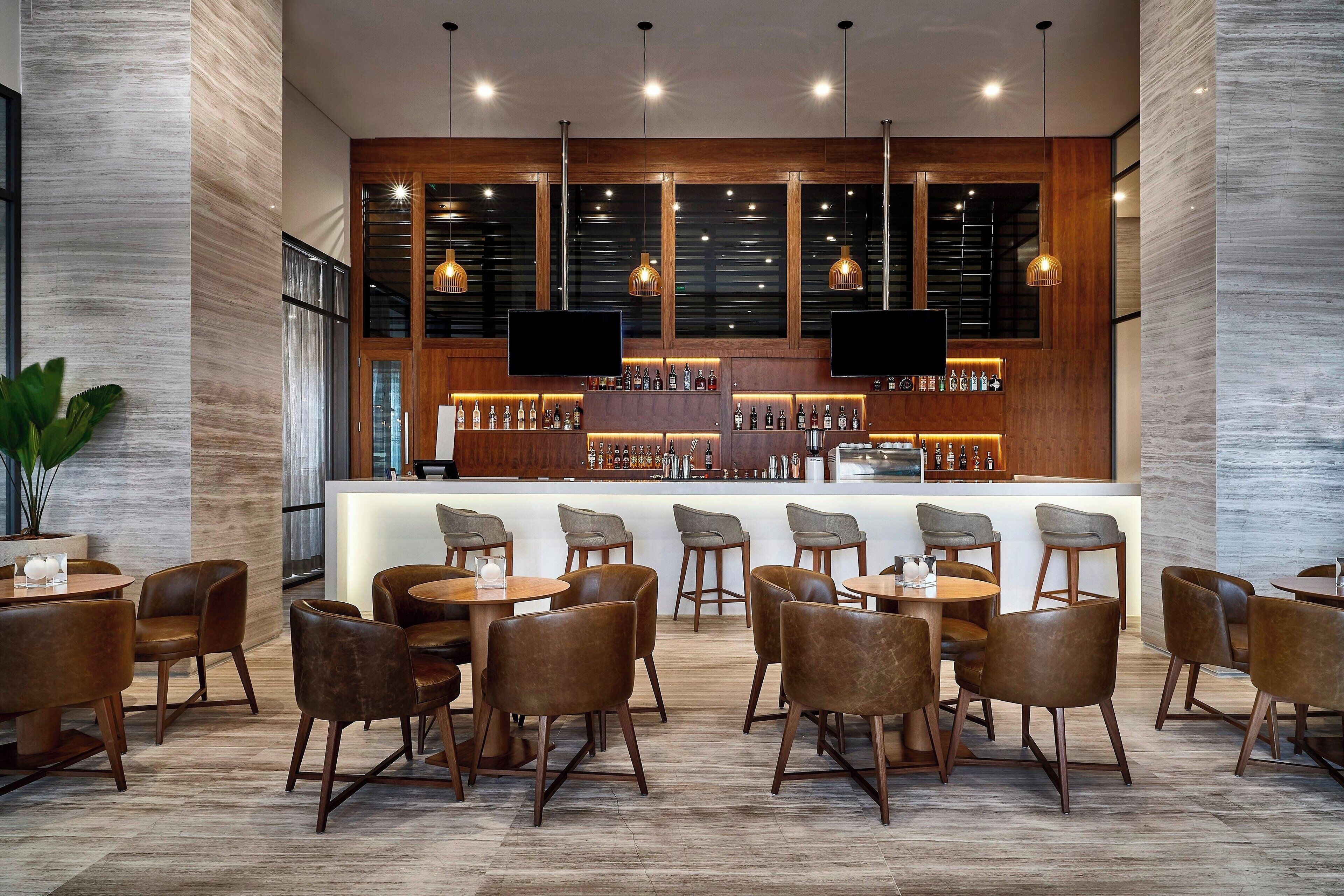 Uma área de bar moderna, com detalhes em madeira, diferentes opções de assento e interior bem iluminado.