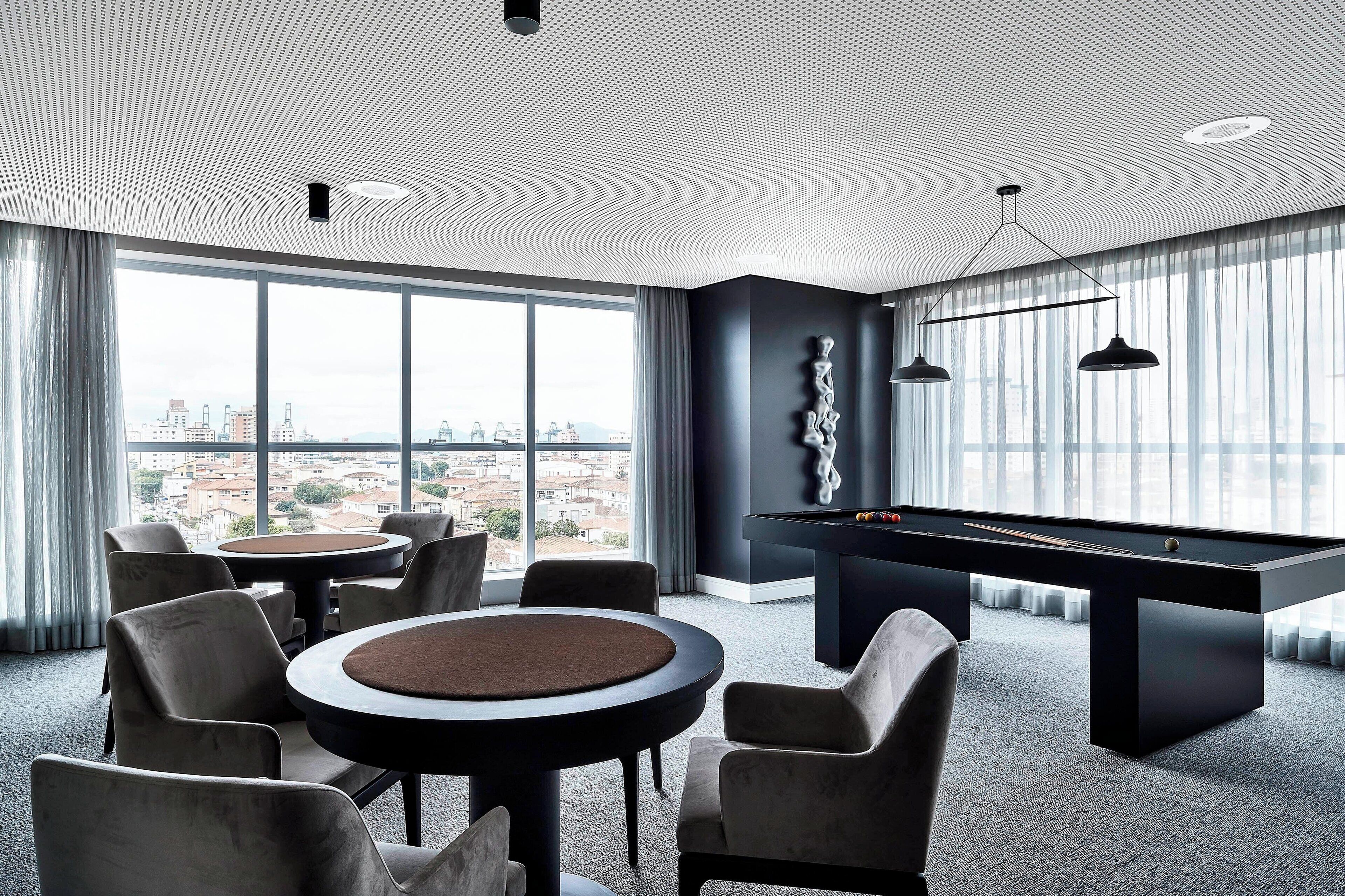 A modern room with a pool table, comfortable seating, and large windows offering a city view.