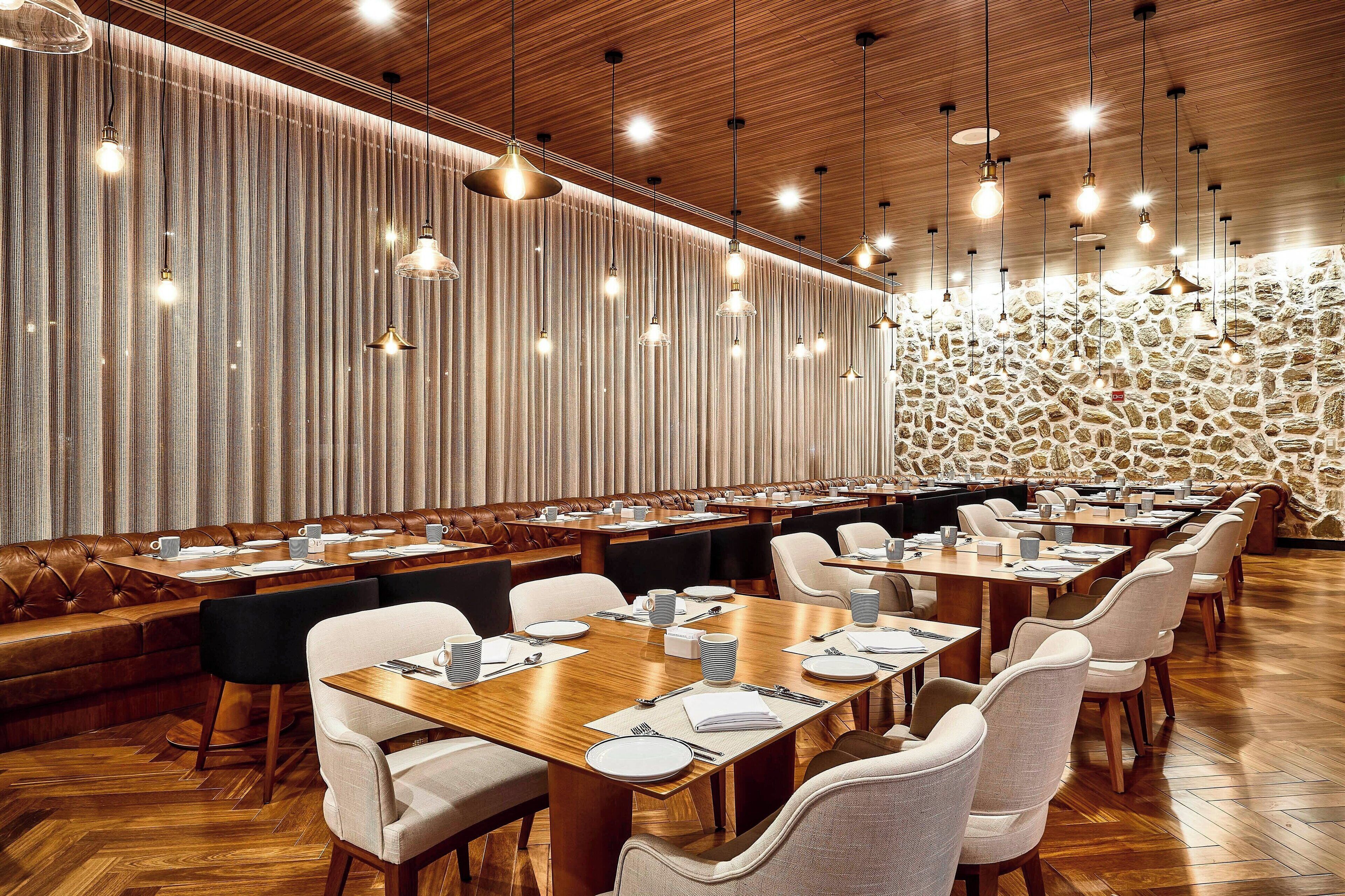 A restaurant with long wooden tables, cushioned booths, and hanging pendant lights.