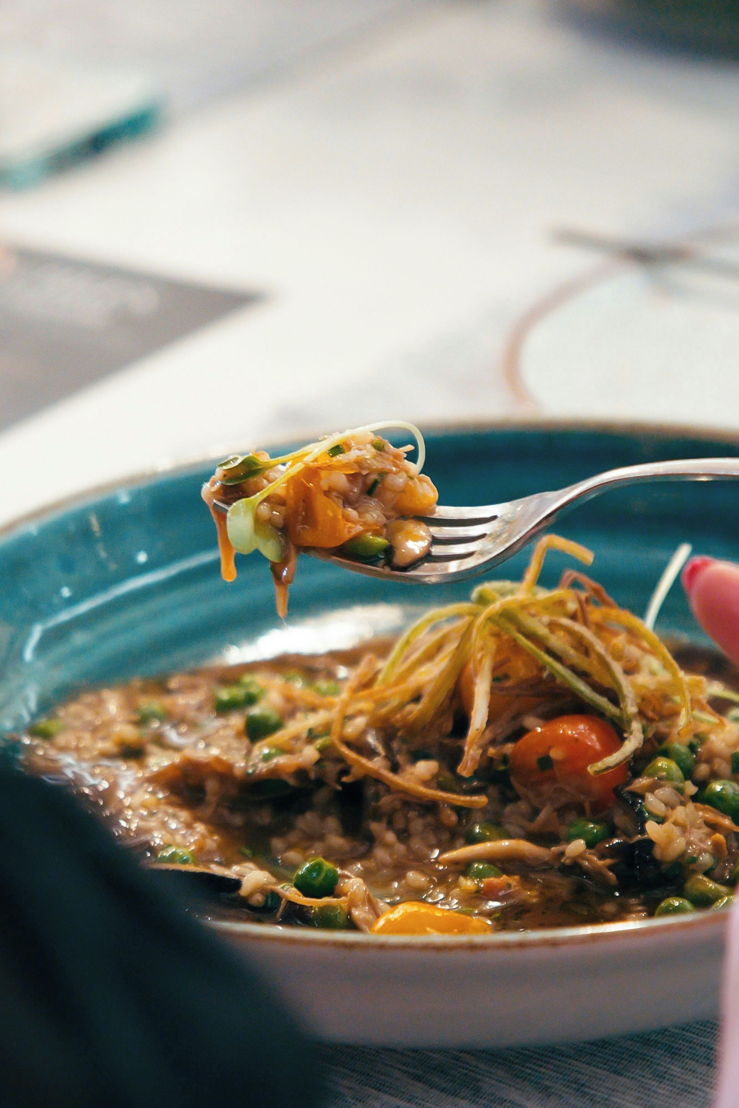 A close-up of a dish with noodles, vegetables, and a piece of chicken being lifted by a fork.
