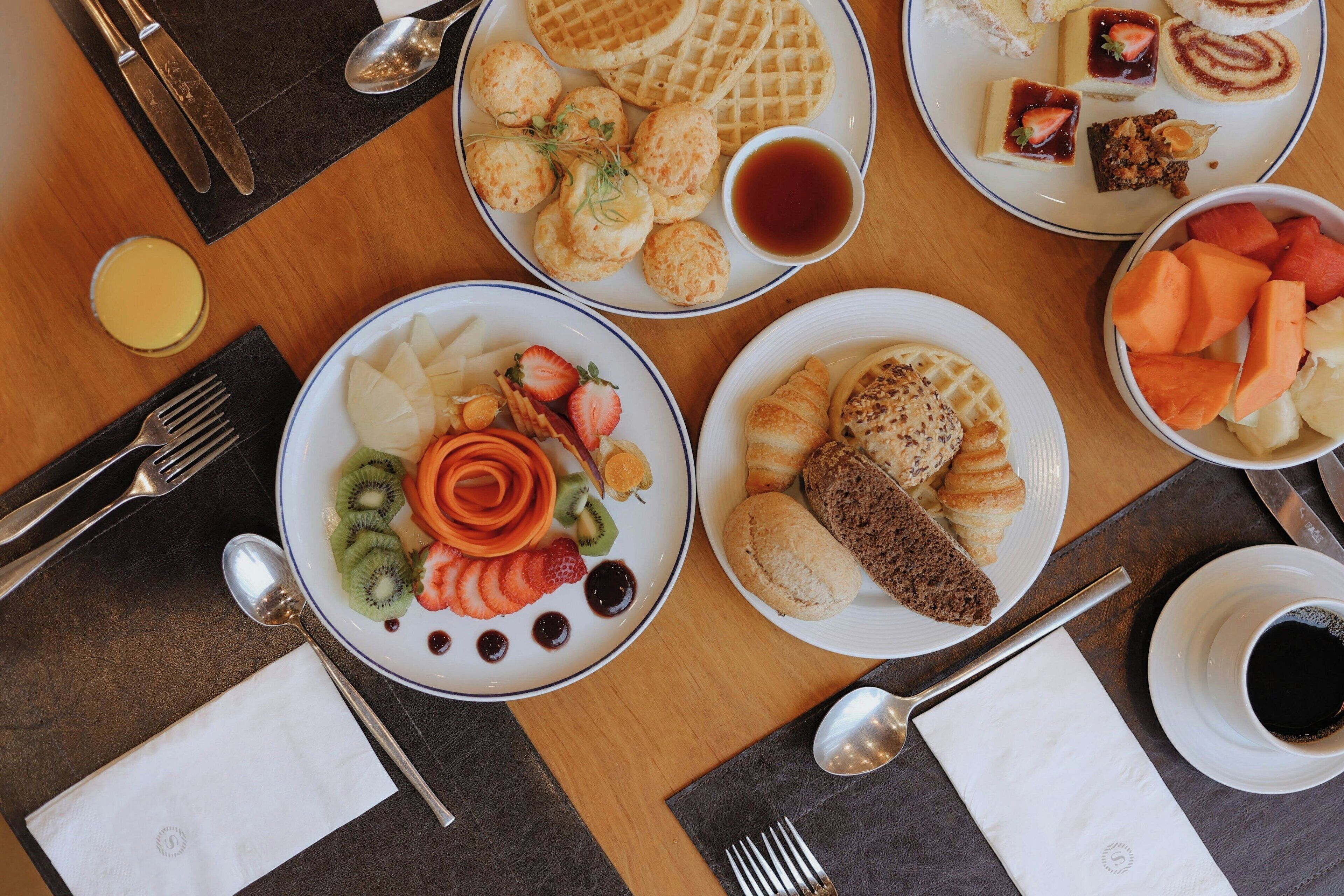 A table set with various breakfast items including waffles, pastries, and fruit.