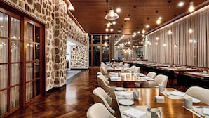A spacious conference room with long tables, wooden floors, stone walls, and modern pendant lighting. - Sheraton Santos Hotel (Santos)