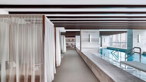 A hotel corridor with a pool on the right, wooden beams on the ceiling, and a bed with a canopy on the left. - Sheraton Santos Hotel (Santos)