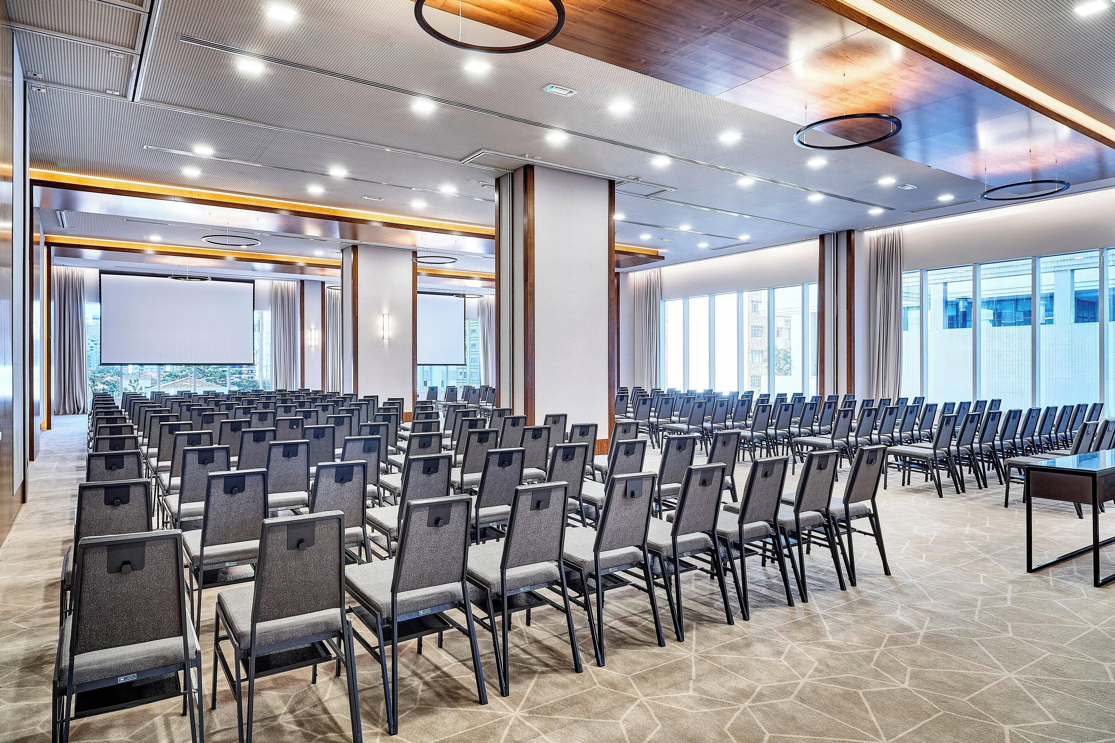 Une salle de conférence avec des rangées de chaises, une grande table et un design moderne au niveau du plafond.
