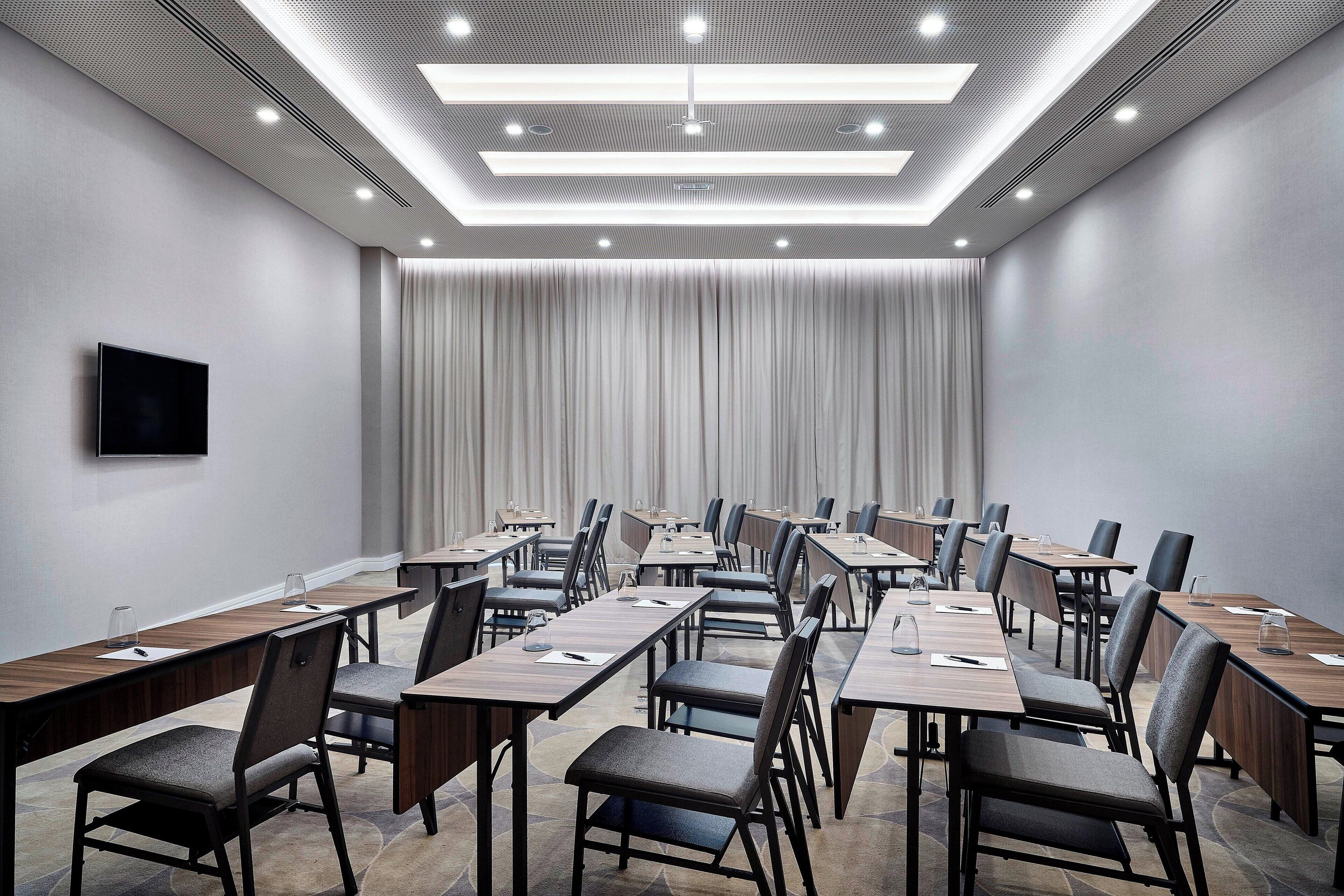 A conference room with long tables, chairs, and a flat-screen TV on the wall.