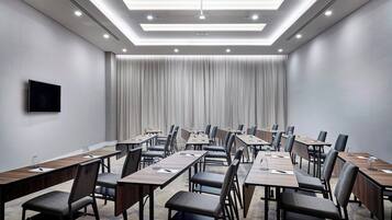A conference room with long tables, chairs, and a flat-screen TV on the wall.