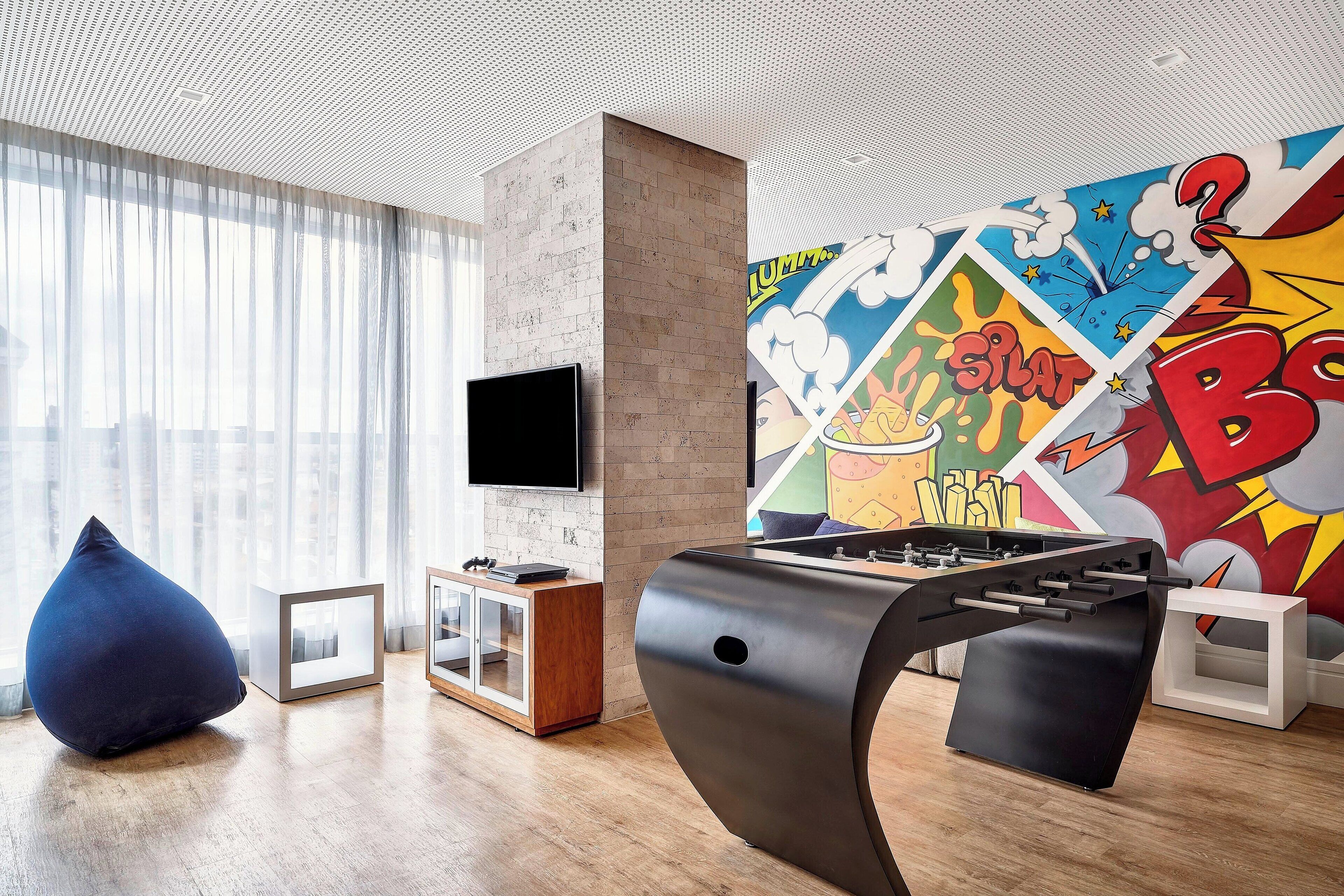 A modern living room with a foosball table, a flat-screen TV, and a colorful comic-style mural.