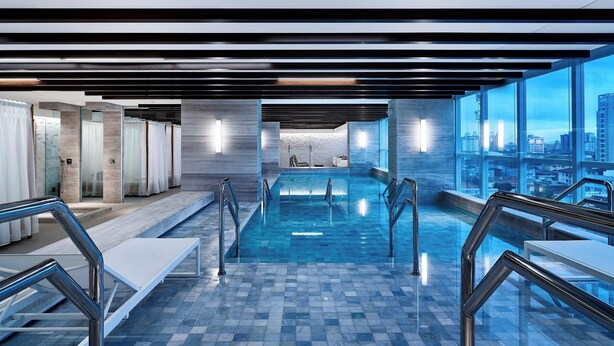 A modern indoor swimming pool with clear glass walls, metal railings, and a city view. - Sheraton Santos Hotel (Santos)