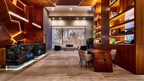 A modern reception area with a marble reception desk, wooden shelving, and a seating area with a sofa and chairs. - Sheraton Santos Hotel (Santos)