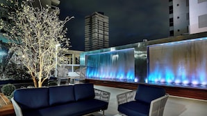 An outdoor seating area with a blue sofa, two armchairs, and a small table. A tree and a building are in the background. - Sheraton Santos Hotel (Santos)