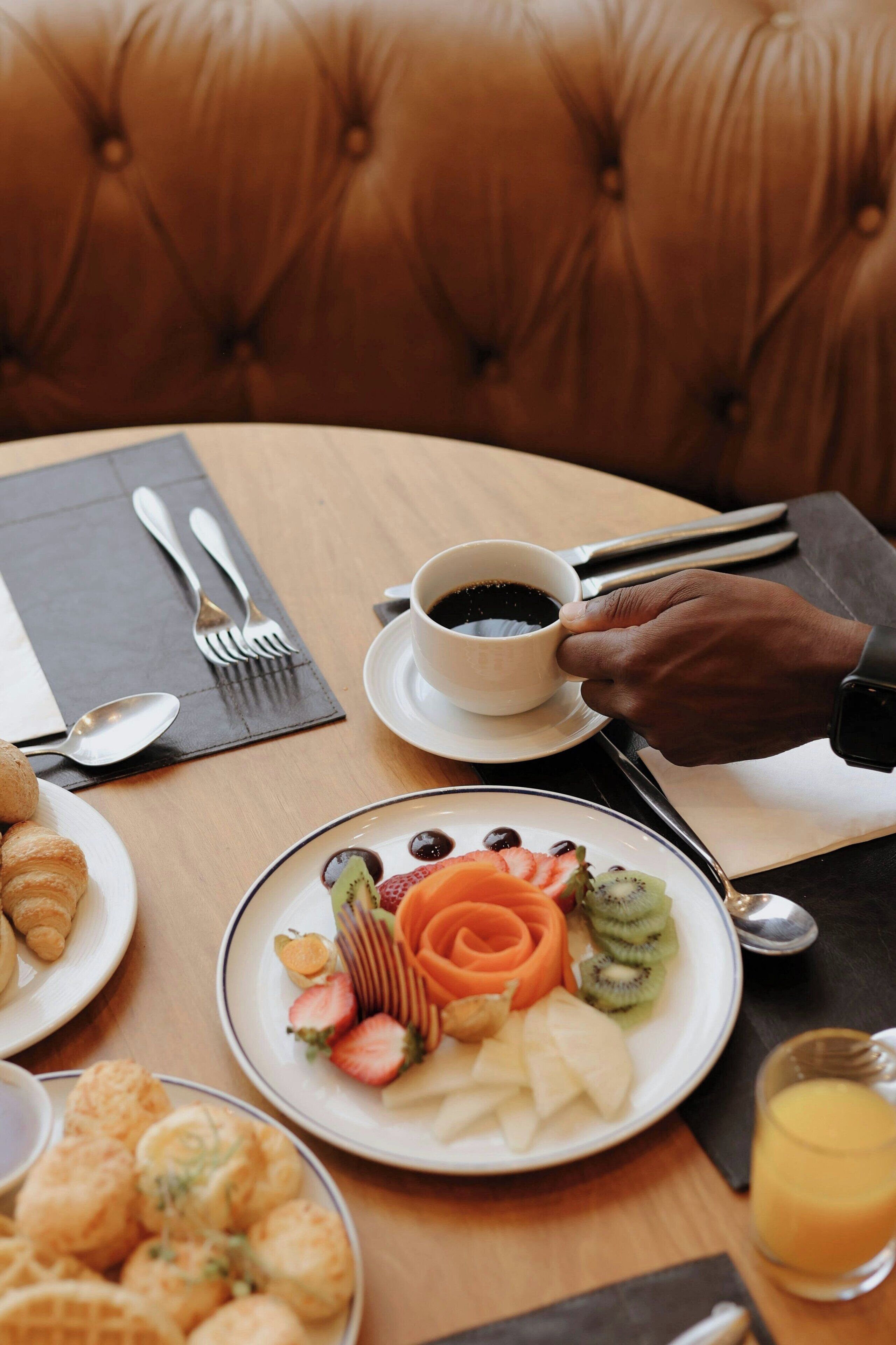 Une table à manger où sont disposés divers aliments pour le petit-déjeuner, notamment des croissants, des fruits et une tasse de café.