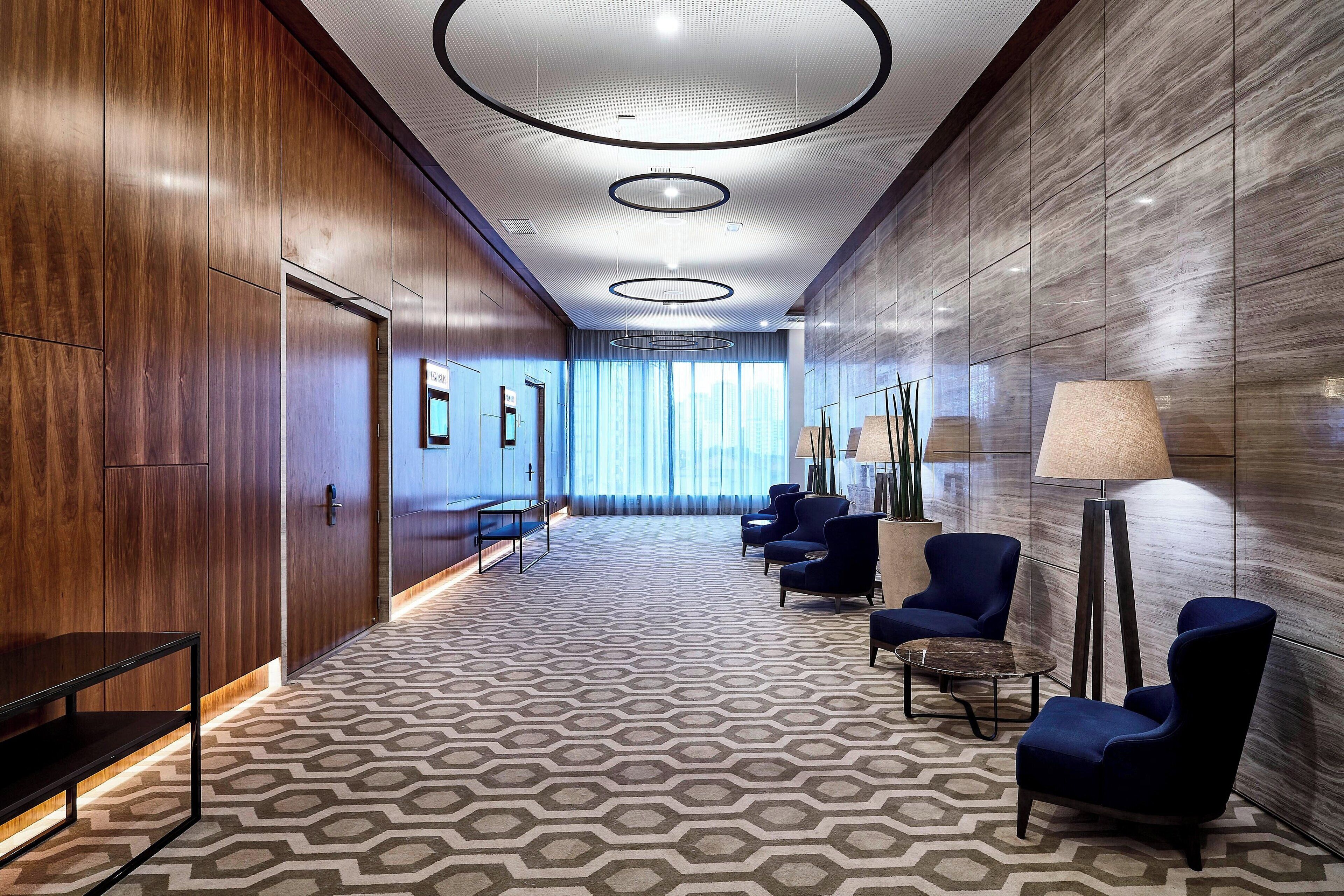 A hotel lobby with a geometric patterned carpet, dark wood paneling, and modern seating.