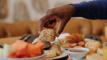 A person reaching for a croissant from a table with various pastries and a bowl of fruit.