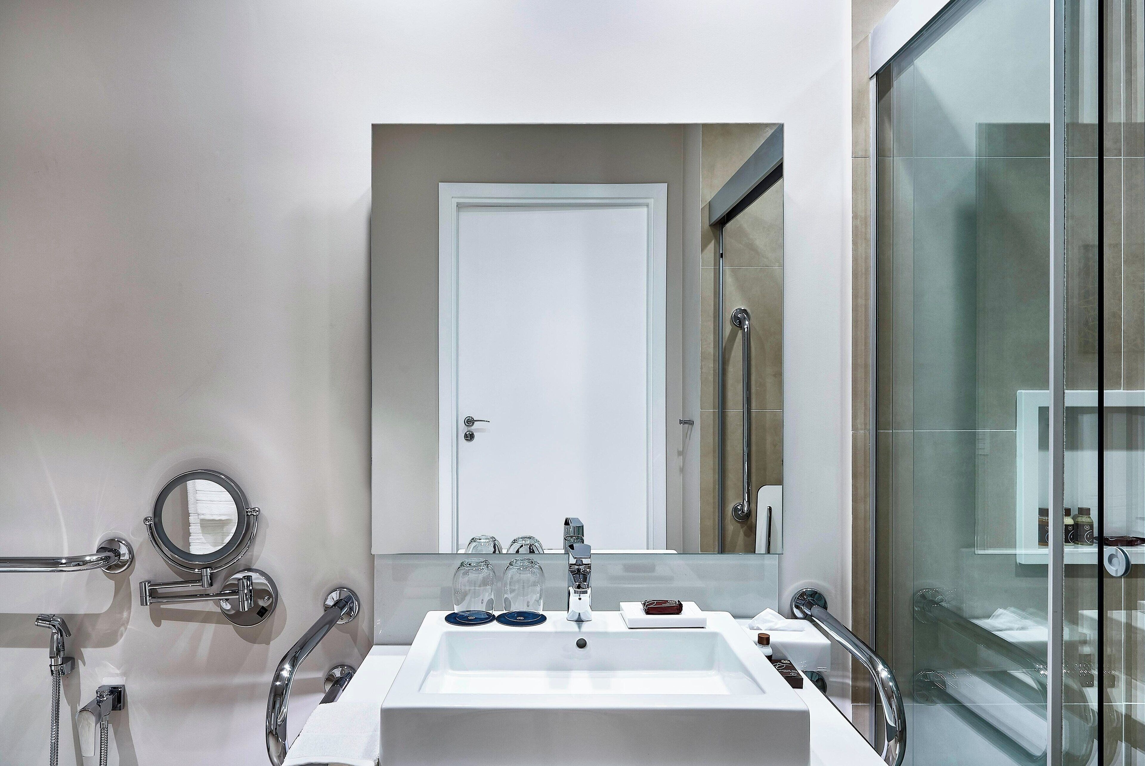 A modern bathroom with a white sink, a mirror, and a glass-enclosed shower.