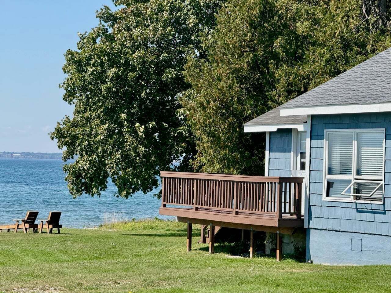 Uma casa com varanda e vista para a água, área gramada e duas cadeiras.