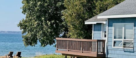 A house with a deck overlooking a body of water, a grassy area, and two chairs.