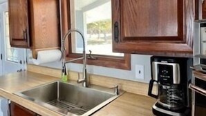 A kitchen with wooden cabinets, a stainless steel sink, and a coffee maker. - Noc's Landing: Sun-Soaked Days & Starry Nights – Your Summer Escape Awaits! (Rapid River)