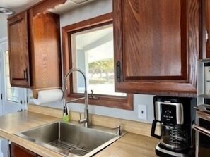 Una cocina con armarios de madera, un lavamanos de acero inoxidable y una cafetera.