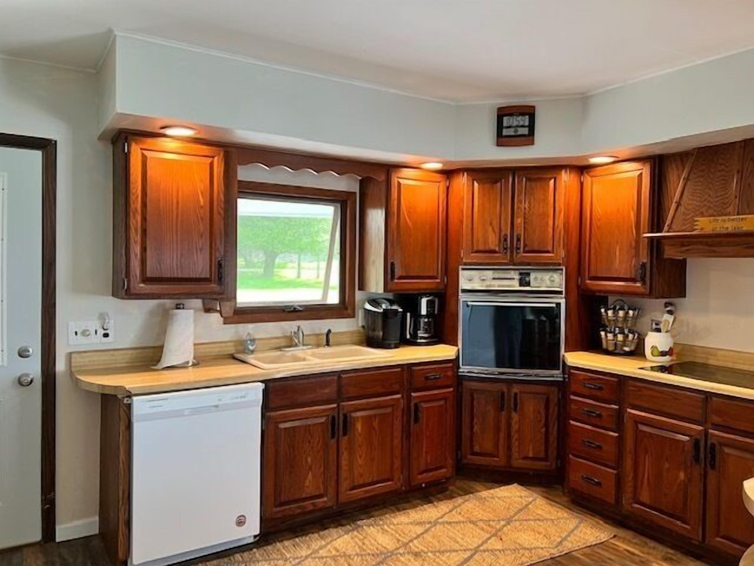 Cocina compacta con armarios de madera, lavavajillas, estufa y ventana con vista a zonas verdes.