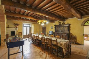 A dining area with a long table, chairs, a foosball table, a fireplace, and a television.