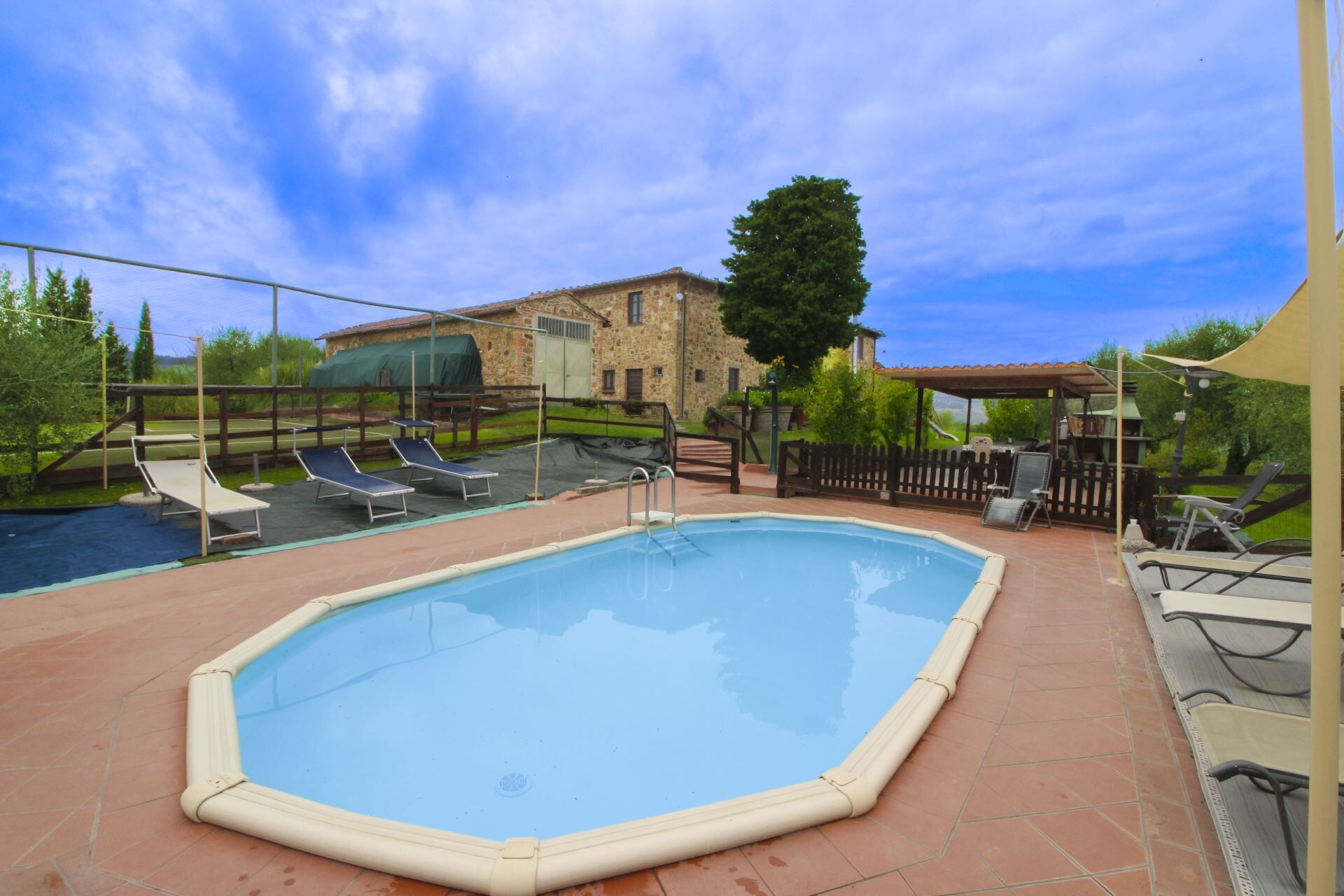 A swimming pool with lounge chairs, a stone building, and a fenced area.