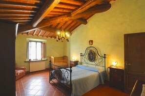 A bedroom with a wooden ceiling, a bed with a headboard, a nightstand, a window with curtains, and a radiator.