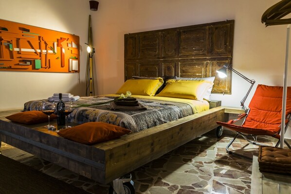 A cozy bedroom with a wooden bed, a chair, a lamp, and a wall art piece.
