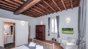 A bedroom with a wooden ceiling, a bed with neatly folded towels, a white sofa, a television, and a wooden cabinet. - Regal Home in Trastevere 3BR (Roma)