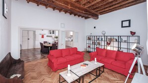 A spacious living room with a high wooden ceiling, two red sofas, a wooden coffee table, and a bookshelf. - Regal Home in Trastevere 3BR (Roma)