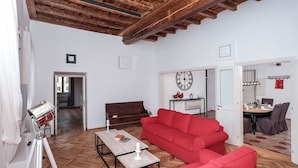 A spacious living area with a wooden ceiling, a red sofa, a wooden coffee table, and a tripod-mounted lamp. - Regal Home in Trastevere 3BR (Roma)