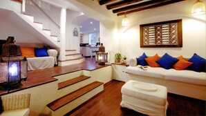 A spacious living area with a staircase leading to an upper floor, a white sofa with colorful cushions, and a decorative lantern.