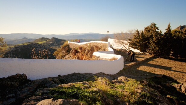A stone pathway leading to a white wall with a person working on it.