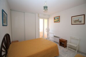 A bedroom with a bed, a chair, a small table, and a radiator. - 3 room apartment with sea view and parking space (Canet-en-Roussillon)