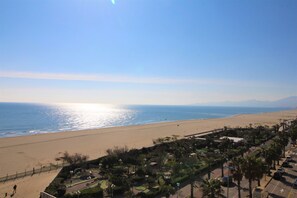 A beach view with a clear sky, a sandy beach, and a parking area with palm trees. - 3 room apartment with sea view and parking space (Canet-en-Roussillon)