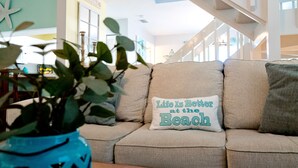 Un canapé beige orné d’un coussin sur lequel on peut lire : « La vie est plus belle à la plage. »