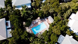 Vue aérienne d’un quartier résidentiel avec une piscine entourée d’arbres et une terrasse délimitée par une clôture.