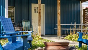 Un bâtiment à l’extérieur bleu, avec une porte et une petite fenêtre sur laquelle est apposée une enseigne. On y voit des chaises bleues et un banc à l’extérieur.