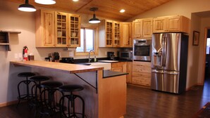 A kitchen with wooden cabinets, stainless steel appliances, a bar area with stools, and a window providing natural light. - Blacktail Inn & Stations (Dillon)