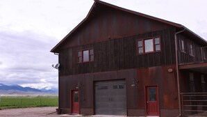 A large, two-story barn with a red door and windows, set against a mountainous backdrop. - Blacktail Inn & Stations (Dillon)
