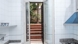 Une cuisine moderne avec des murs recouverts de carreaux blancs, un plan de travail en granit, un four encastré et une vue sur un escalier menant à l’extérieur.